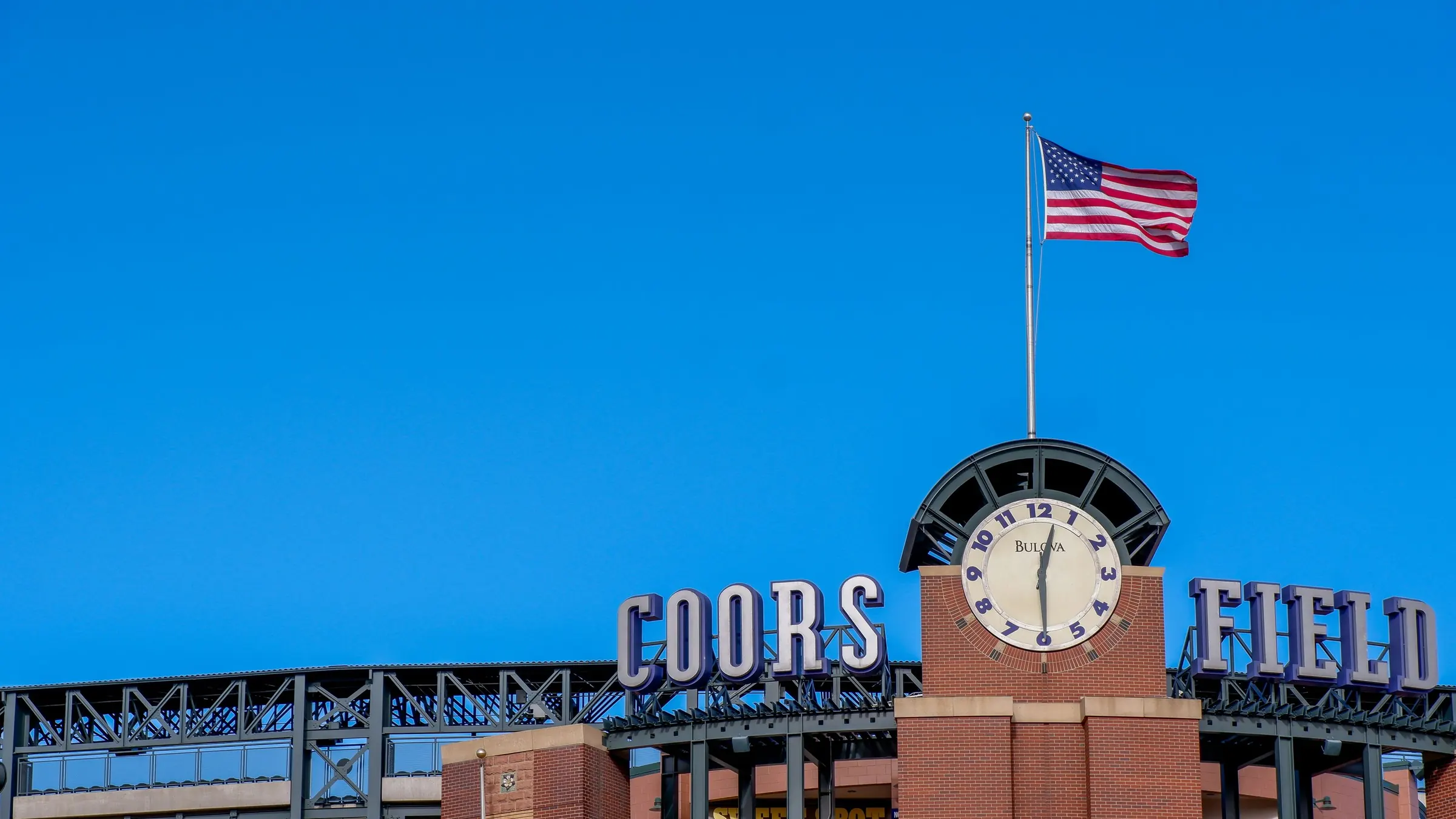 The Coors Field clock tower and flag against a clear Denver sky